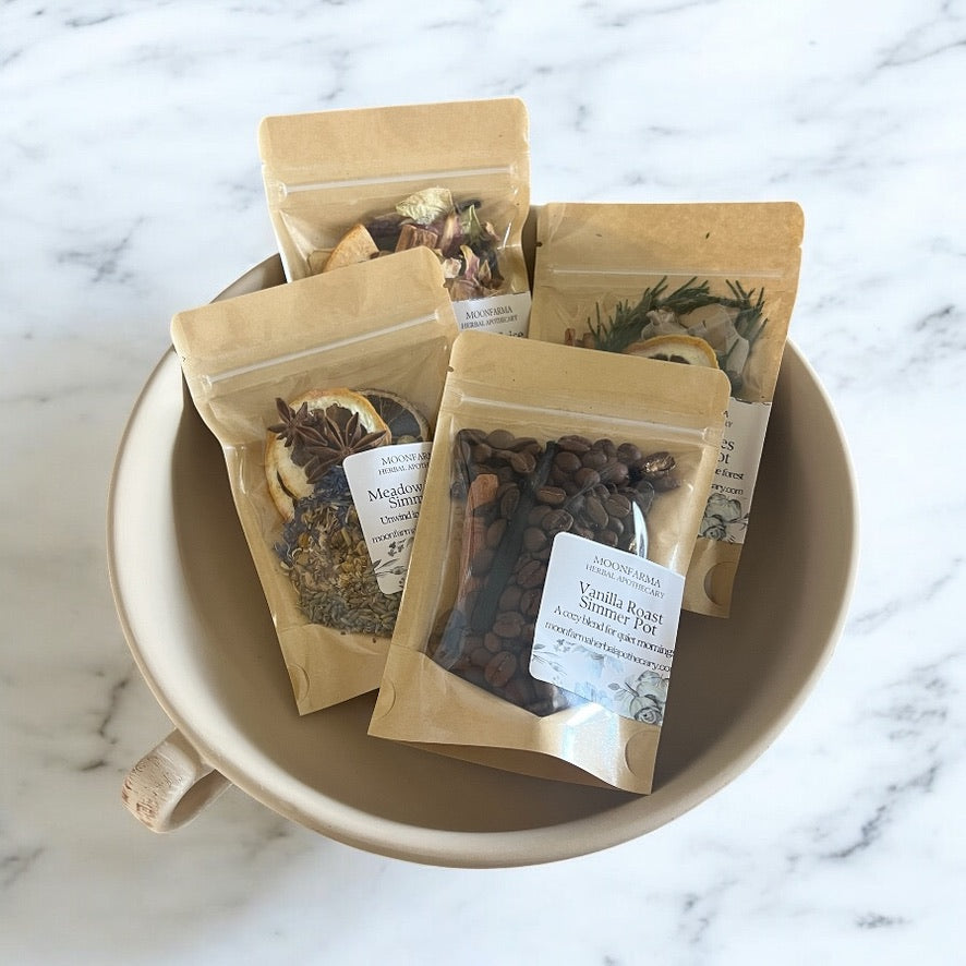 Simmer pot blend pouches in kraft paper, assorted dried botanicals in a white bowl.