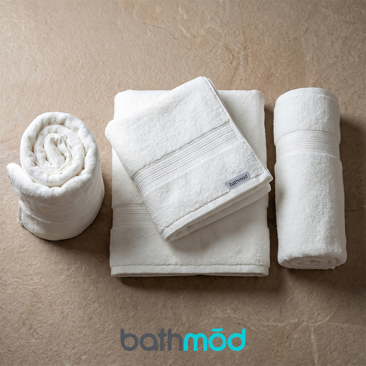 White bath towel four-pack set, folded and rolled with stitched hems and logo tag.