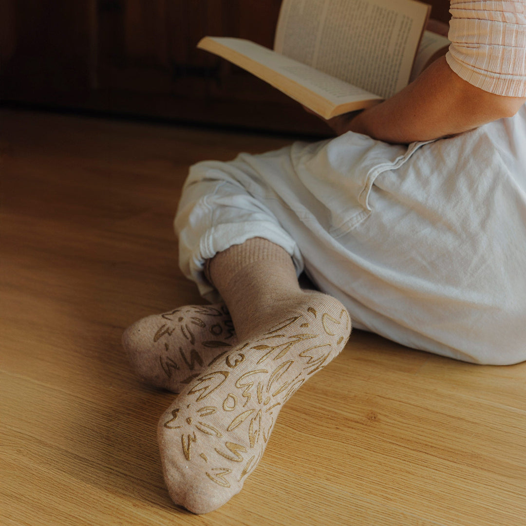 Brown crew socks with leafy non-slip print, worn with feet on the floor