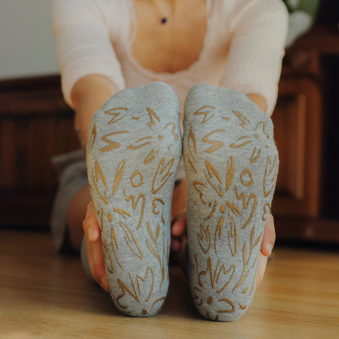 Two grey crew socks with gold floral non-slip grip on underside