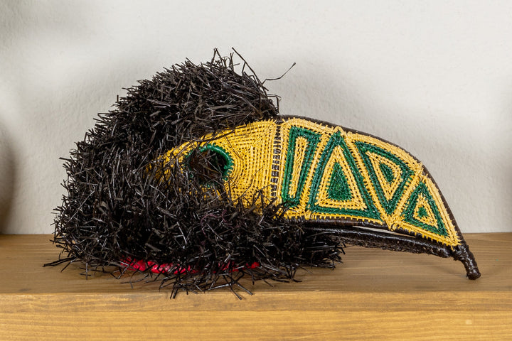 Side view of toucan mask with black shag body, yellow beak, and green triangle stitching