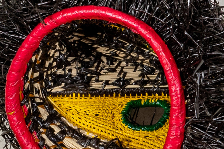 Toucan mask close-up with red rim, green eye, and woven yellow face panel