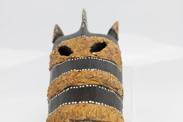 Close-up of horned giraffe mask face with black base and gold patterned bands