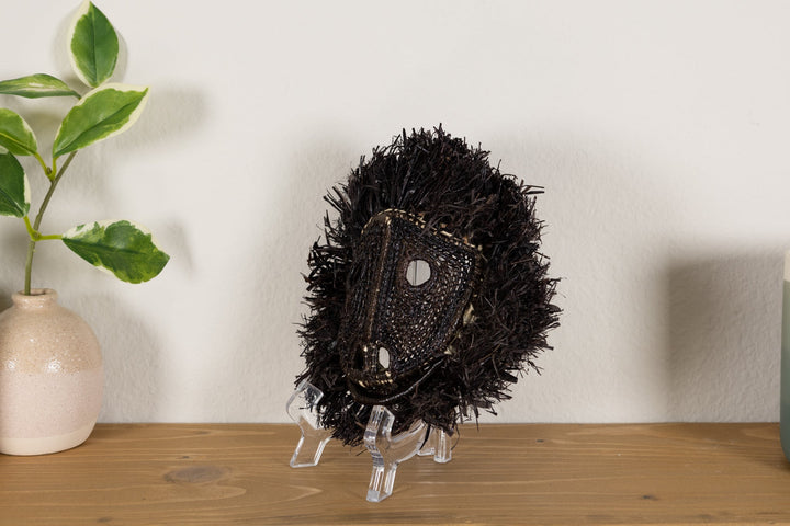 Spiky black howler monkey mask shown from the side on a clear display stand