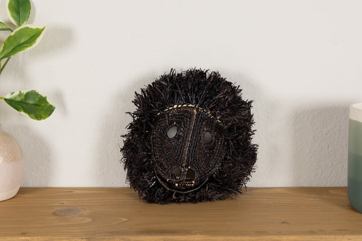 Black howler monkey mask with spiky fur and detailed woven muzzle on a display stand