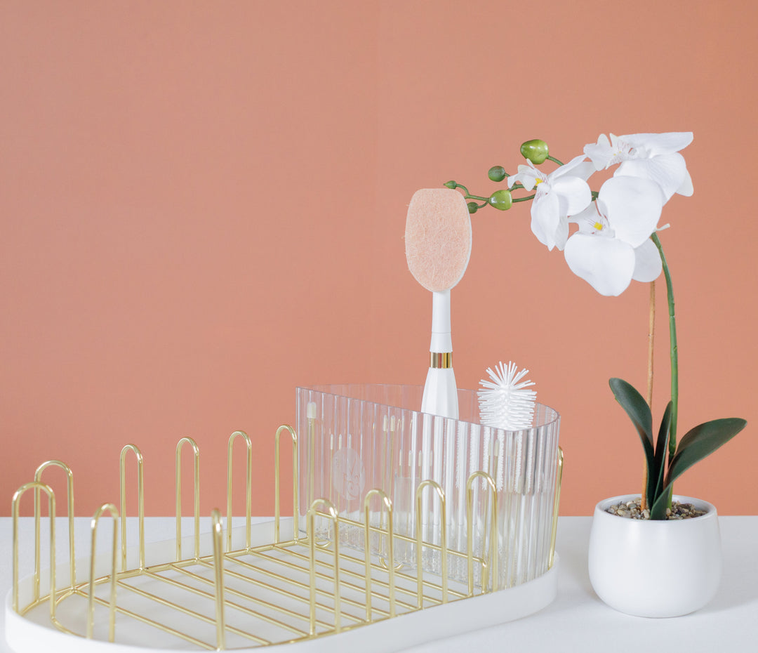 Gold countertop dish drying rack with bottle brush, glassware slots, and floral decor