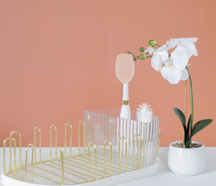 Gold countertop dish drying rack with bottle brush, glassware slots, and floral decor
