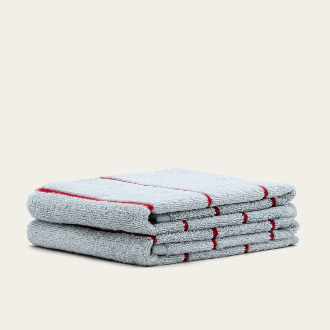 Folded gray cotton towels with red striped edges stacked neatly on a light background.