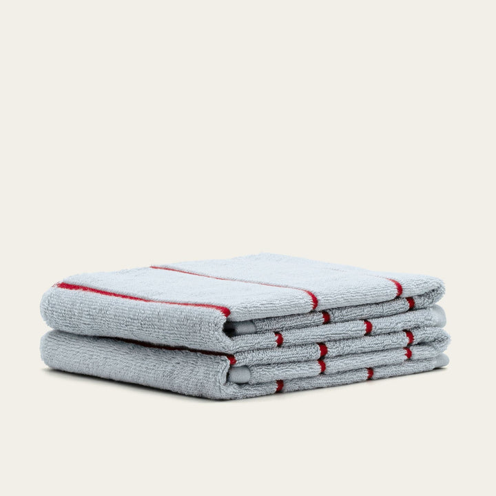 Folded gray cotton towels with red striped edges stacked neatly on a light background.