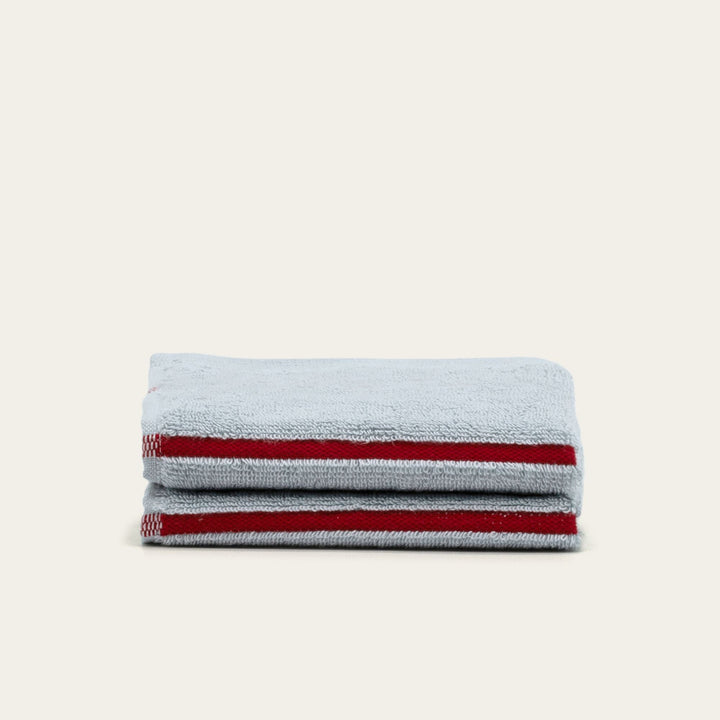 Stack of gray cotton towels with red stripe accents, folded and neatly aligned.