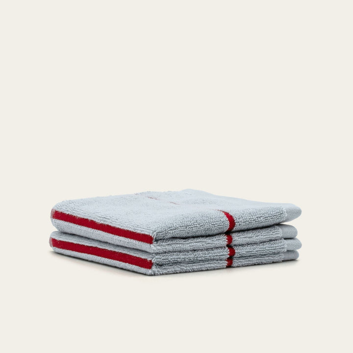 Two stacked gray cotton towels with red striped borders, folded with rolled corner.