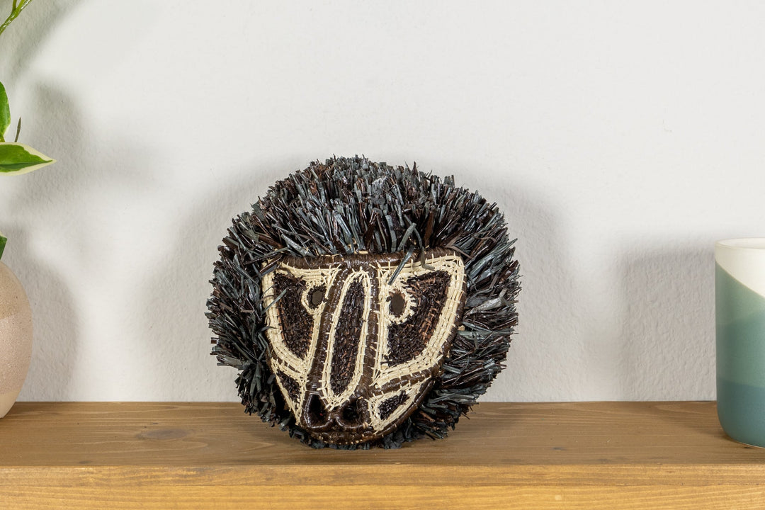 Colobus monkey mask close-up on clear stand with dark fringe and cream embroidered face