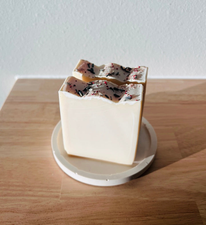 Handmade off-white soap bar with dark speckles and red herb bits on a dish