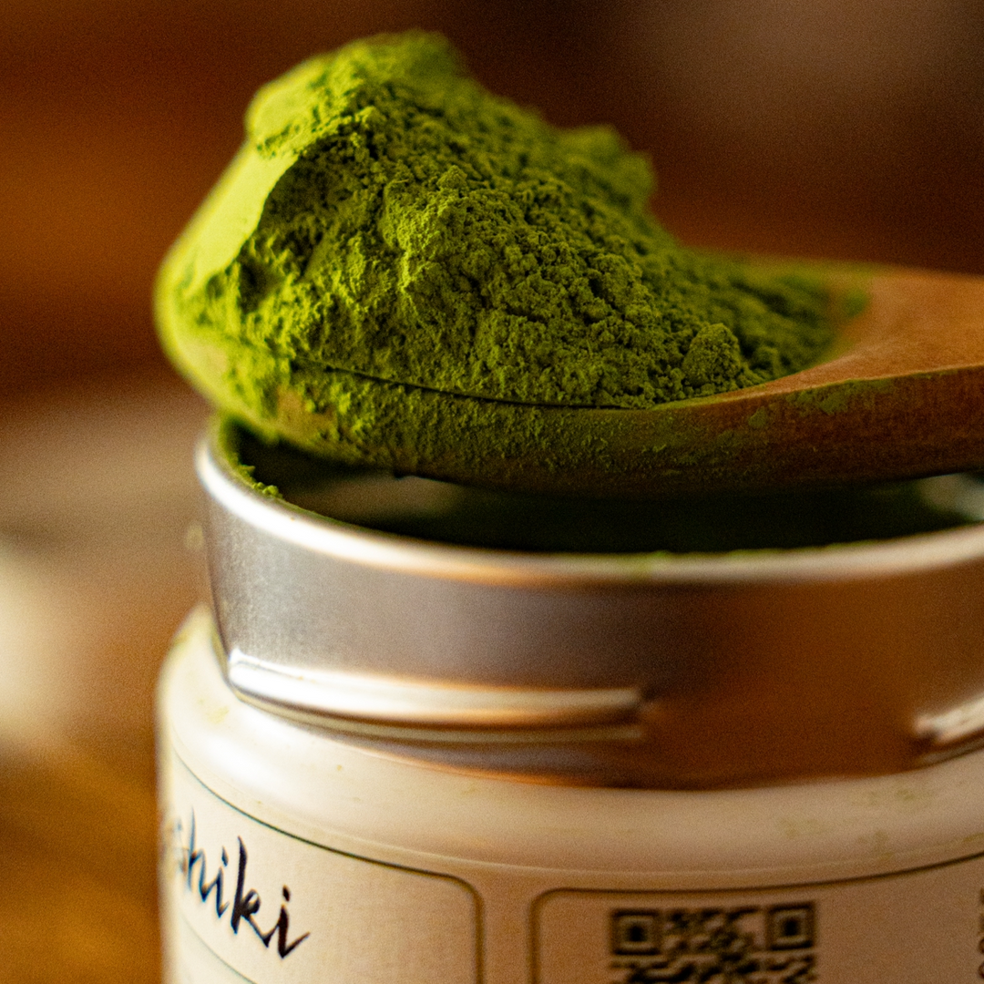 Green matcha powder mound on a spoon above a matcha tin