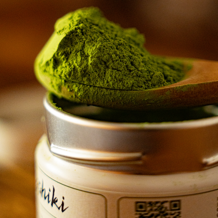 Green matcha powder mound on a spoon above a matcha tin