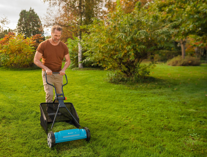 Blue cylinder lawnmower being pushed by a person on a lawn.