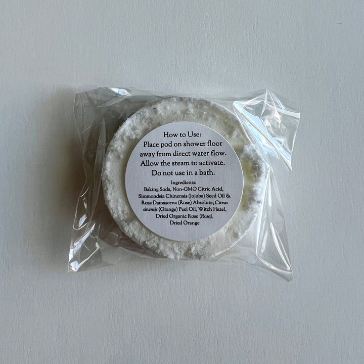 Circular shower steamer in clear plastic wrap with usage label on top