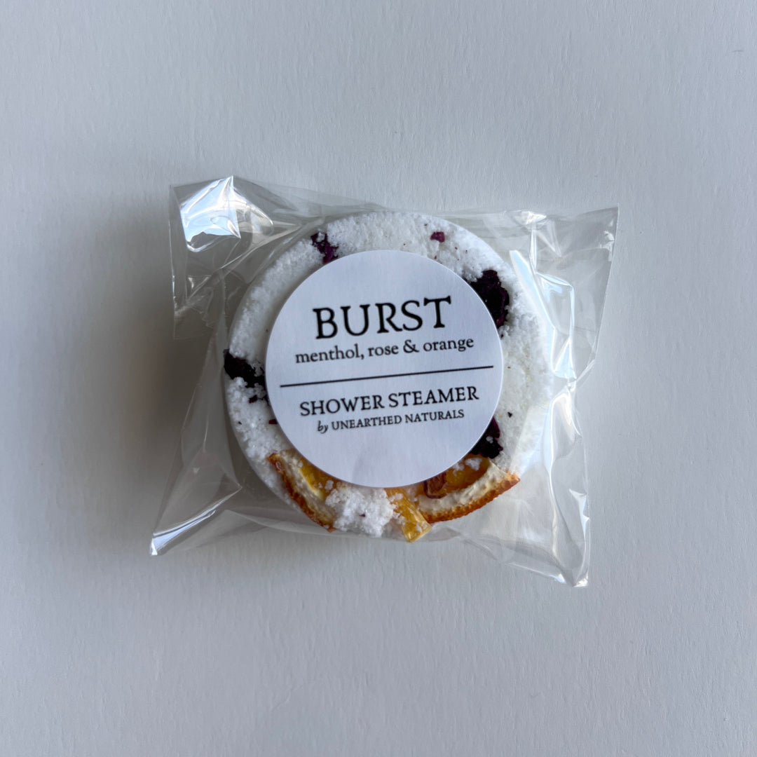 Individually wrapped circular shower steamer with white label and citrus flecks