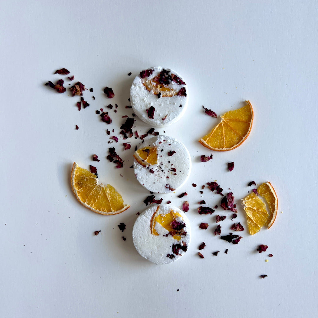 Round white shower steamer tablets with dried citrus pieces scattered around