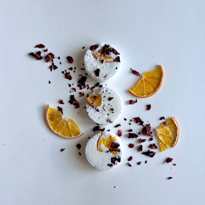 Round white shower steamer tablets with dried citrus pieces scattered around