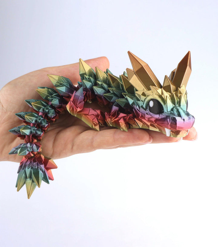 Articulated crystal baby dragon fidget toy held in hand, gold and green facets