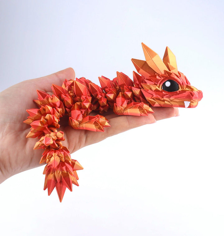 Articulated crystal baby dragon fidget toy held in hand, orange-red facets