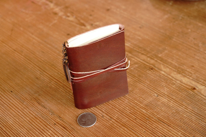 Distressed leather mini journal with wrap strap, open edge visible, dark red-brown