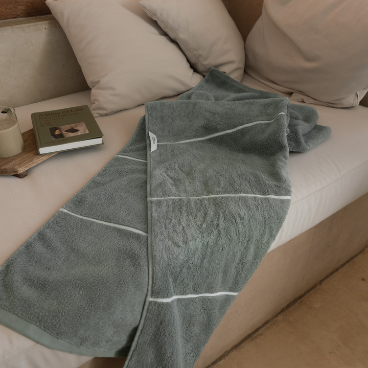 Sage-green cotton towels with white border trim folded on a couch