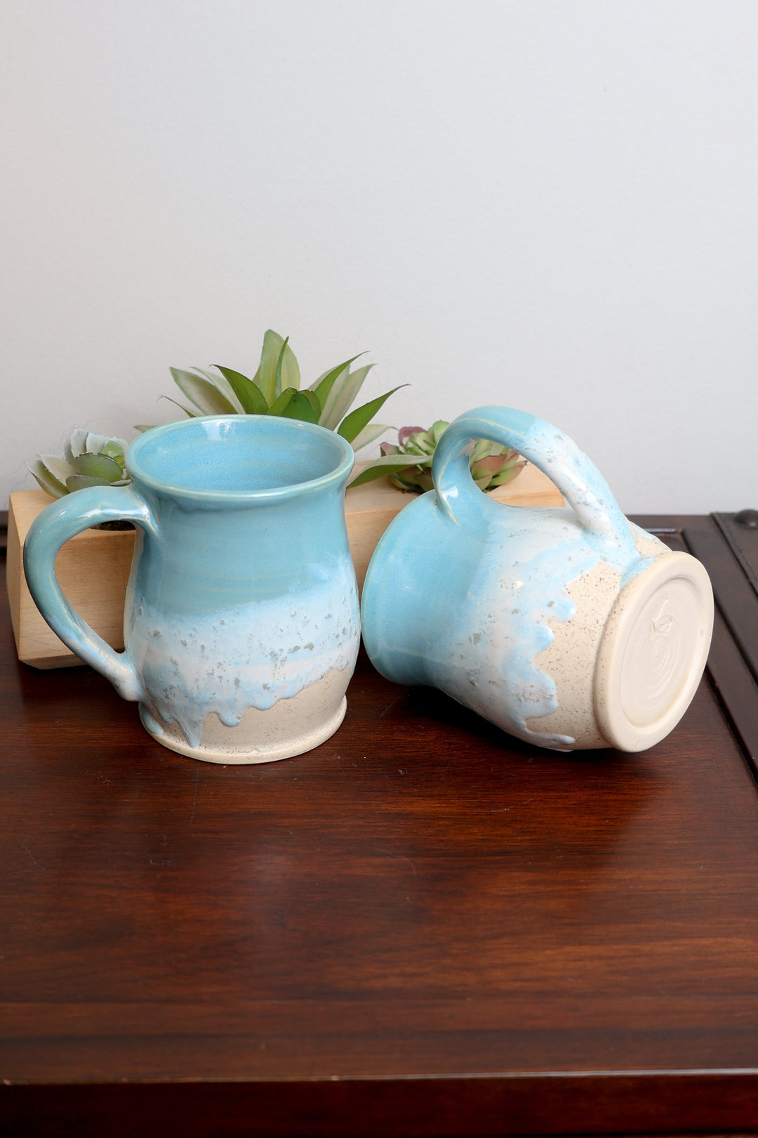 Pair of blue ceramic mugs with speckled coastal glaze, one showing interior and spout