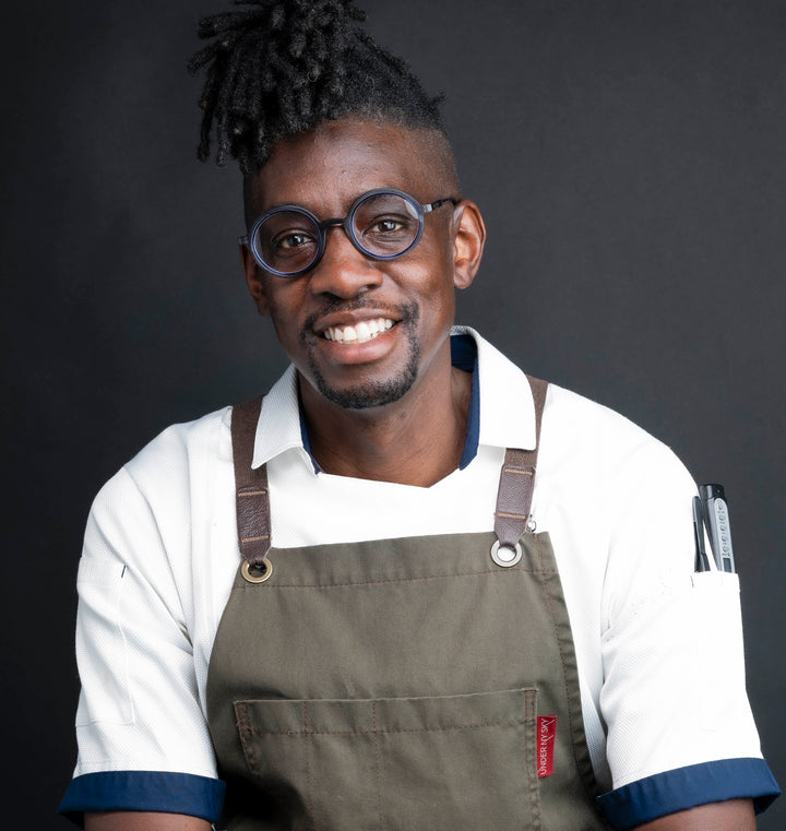 Chef in white shirt wearing brown apron with spice logo patch.
