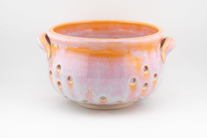 Handmade ceramic berry strainer bowl in orange glaze with two side handles and vent holes