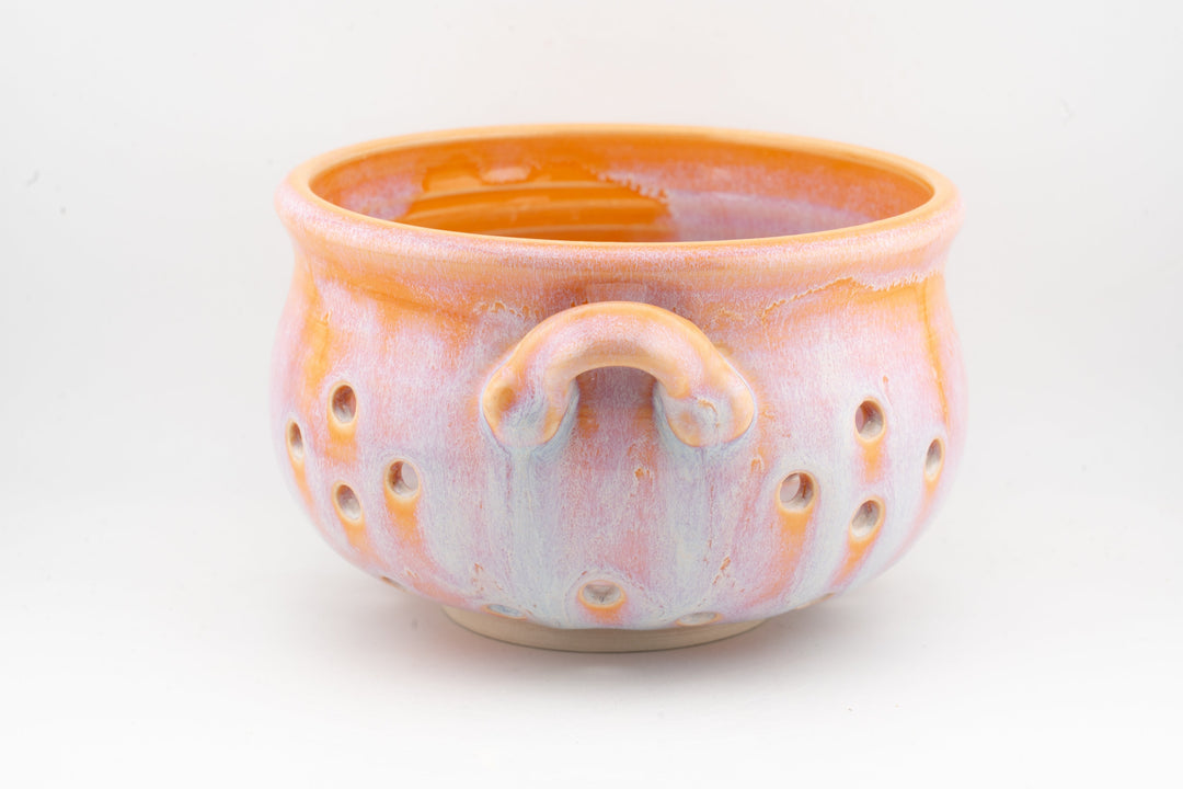Handmade ceramic colander bowl with orange glaze, arched handle loop, perforated side holes
