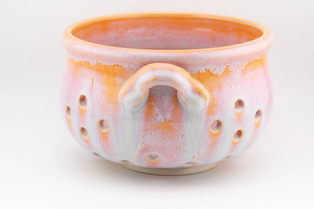 Handmade ceramic colander bowl with orange rim glaze, central handle loop, perforated sides