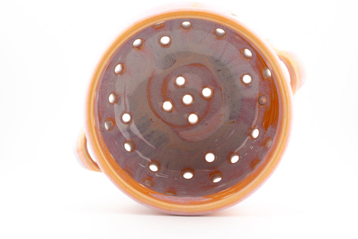 Inside view of handmade ceramic colander bowl with dark glazed base and orange rim
