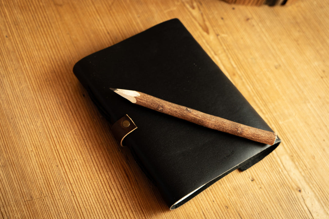 Black leather notebook with wooden pencil laid across the cover