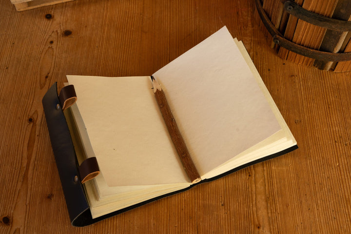 Open black leather journal with white pages and wooden pencil in the cover sleeve
