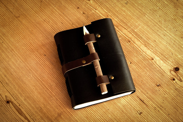 Black leather journal with attached wooden pencil, wrapped with brown strap details