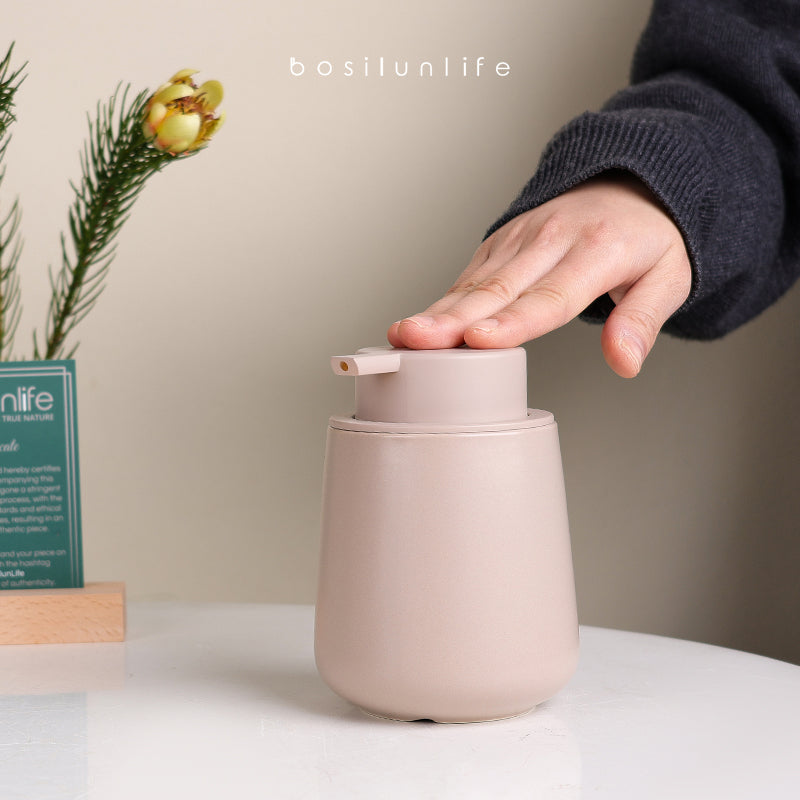 Large ceramic liquid soap dispenser, light pink body with pump, hand shown
