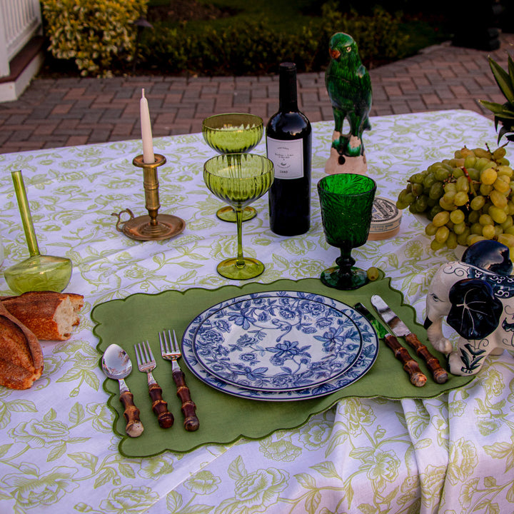 Green botanical-imprinted goblets on a decorated outdoor table with bottles and grapes.