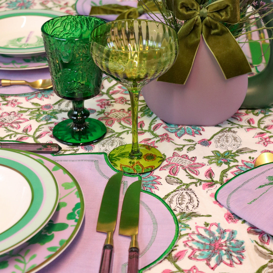 Green botanical-imprinted goblets on a table with gold wine glass and linens.