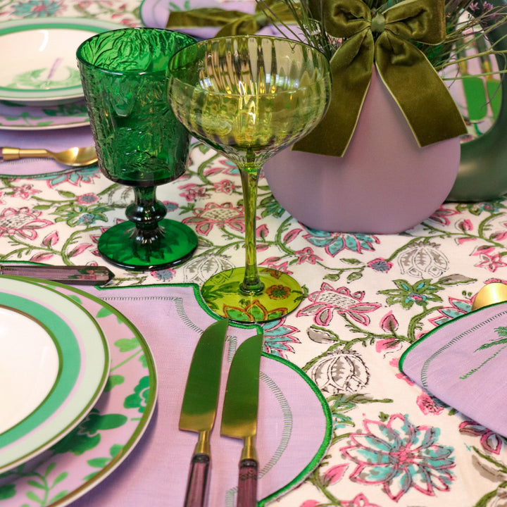 Green botanical-imprinted goblets on a table with gold wine glass and linens.