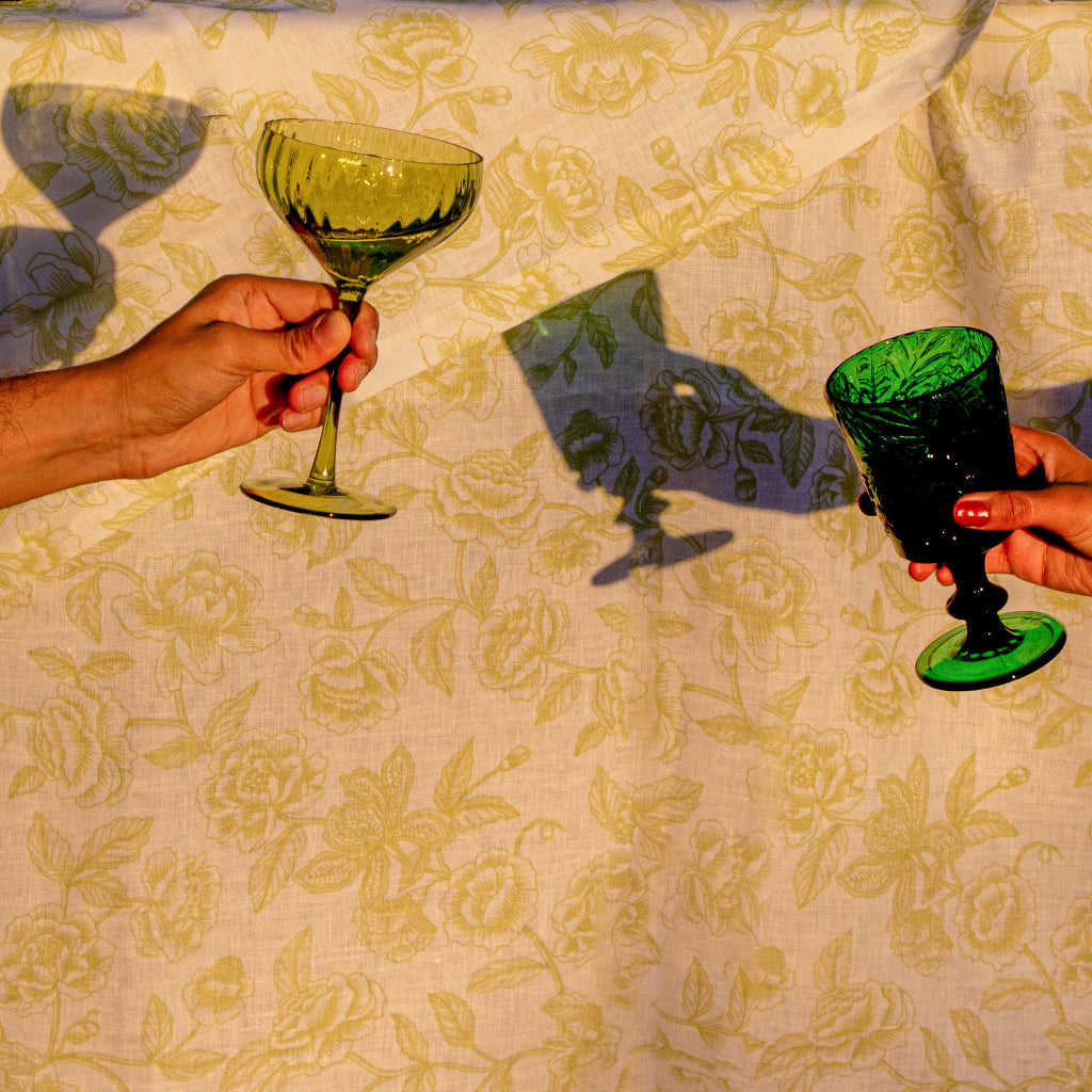 Hand holding a green botanical-imprinted glass goblet with stem and round base.