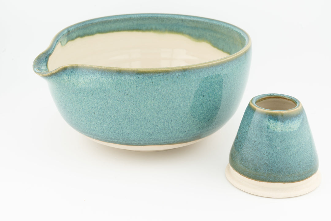 Turquoise ceramic matcha bowl with small spout and matching whisk stand.