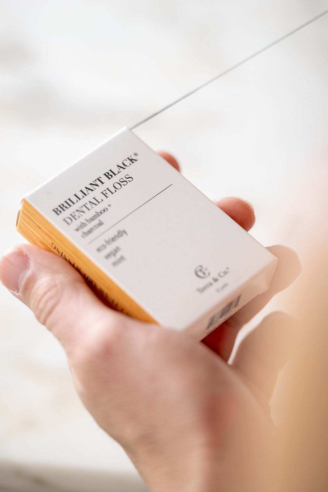 Brilliant Black® dental floss mini box with bamboo charcoal, held in a hand