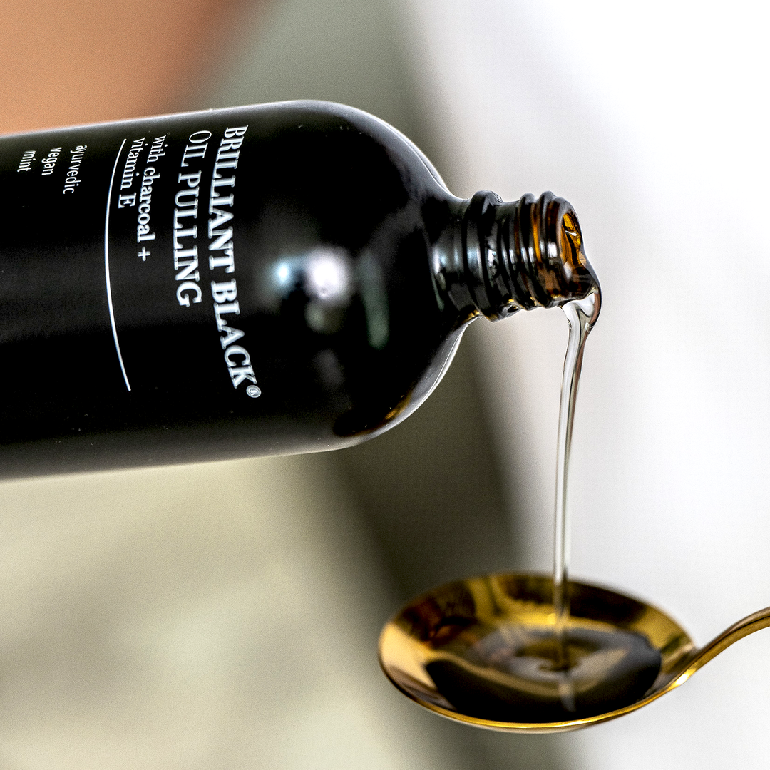 Black oil pours from a Brilliant Black oil pulling bottle into a spoon