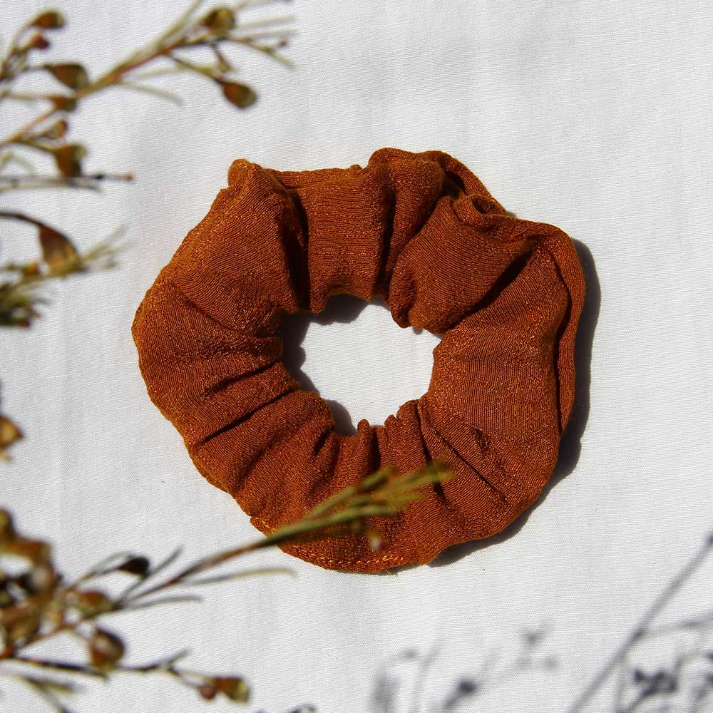Rust-colored scrunchie with gathered fabric and elastic loop shape.