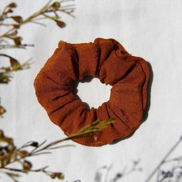 Rust-colored scrunchie with gathered fabric and elastic loop shape.