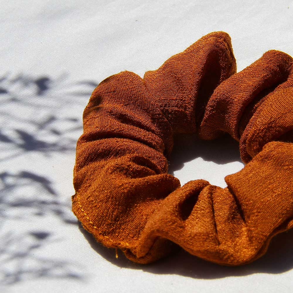 Rust scrunchie with textured fabric and ruched, scrunched elastic band.