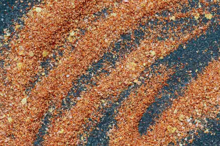 Red-orange spice seasoning powder with fine granules on dark surface