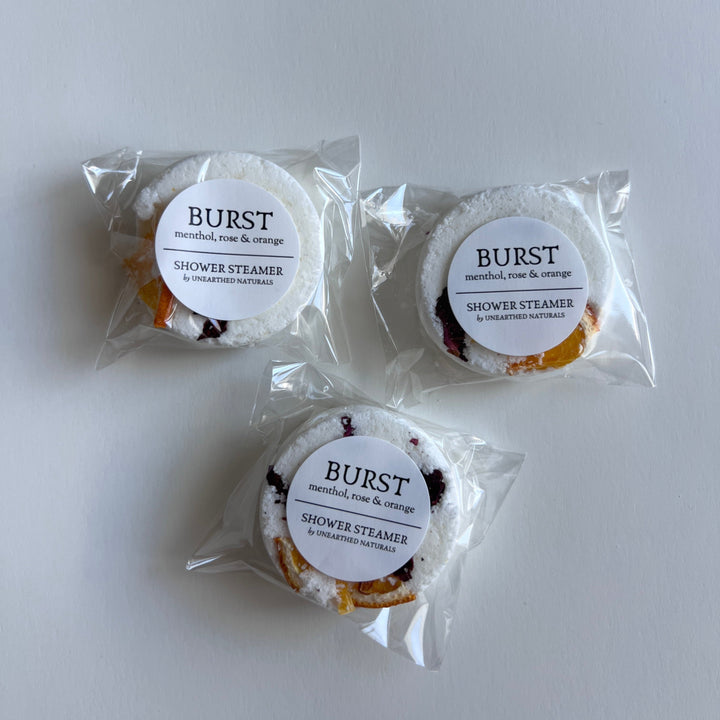 Three wrapped circular shower steamers arranged on a surface